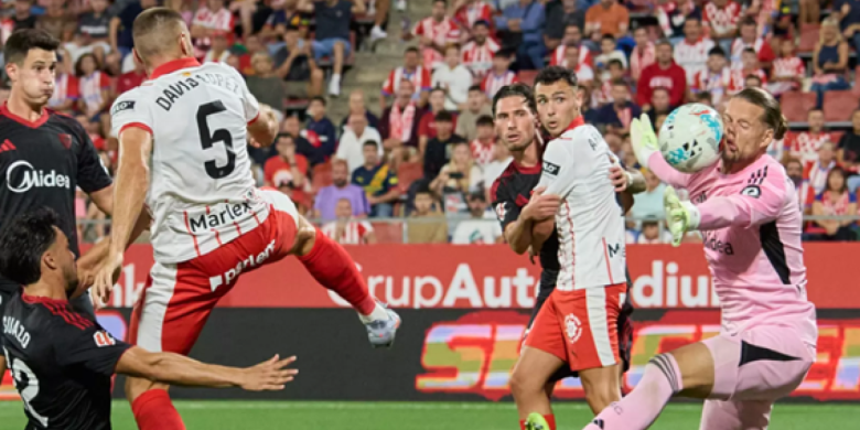 "Aturada descomunal", capta un instant precís i impactant d'un partit de futbol entre el Girona FB i el Sevilla, amb el porter Ørjan Nyland rebent l'impacte de la pilota.